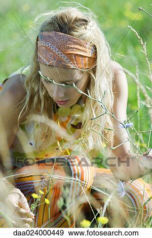 Stock Photo - Young woman crouching to pick flowers in field, close-up. Fotosearch