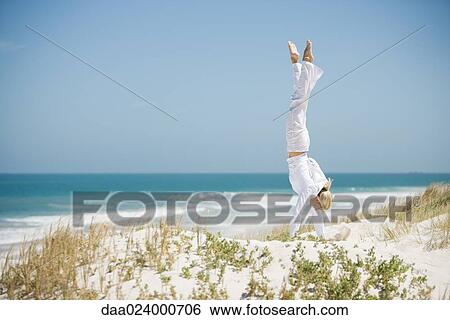 Young woman doing handstand in dunes, ocean in background View Large Photo Image Stock Photograph - Young woman doing handstand in dunes, ocean in background. Fotosearch