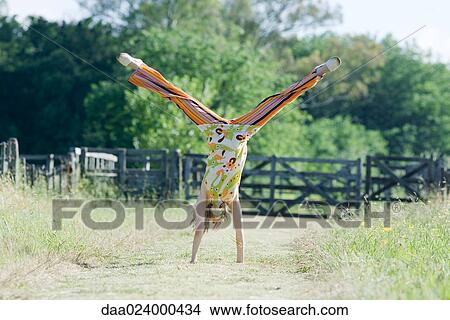 Picture - Young woman doing handstand in rural field. Fotosearch
