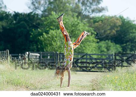 Stock Image - Young woman doing handstand in rural field. Fotosearch