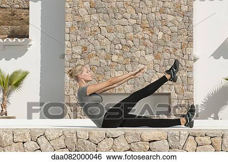 Stock Photograph - Young woman doing sit-ups outdoors, side view. Fotosearch