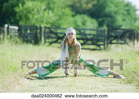 Stock Image - Young woman doing splits in rural field, smiling at camera. Fotosearch