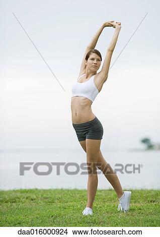 Picture - Young woman doing stretching exercises by lakeside. Fotosearch