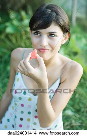 Young woman eating piece of fruit, smiling, high angle view View Large Photo Image Picture - Young woman eating piece of fruit, smiling, high angle view. Fotosearch