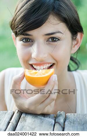 Stock Image - Young woman eating slice of orange. Fotosearch