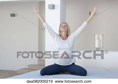 Stock Photo - Young woman exercising on bed with arms raised. Fotosearch