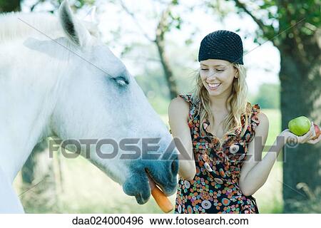 Young woman feeding horse a carrot, apples in hand View Large Photo Image Stock Photograph - Young woman feeding horse a carrot, apples in hand. Fotosearch