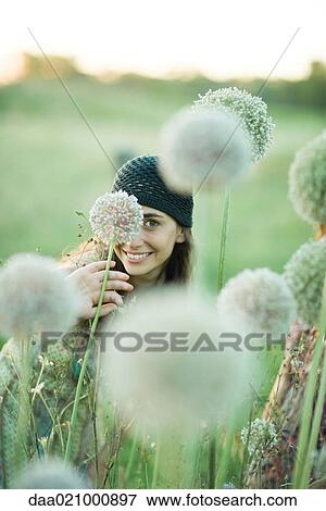 Stock Photo - Young woman hiding behind allium flower, looking at camera. Fotosearch