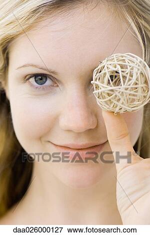 Young woman holding ball in front of one eye, smiling at camera, portrait View Large Photo Image Stock Photo - Young woman holding ball in front of one eye, smiling at camera, portrait. Fotosearch