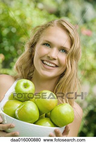 Stock Image - Young woman holding bowl of apples. Fotosearch