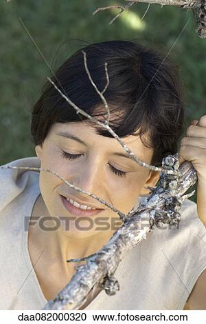 Stock Image - Young woman holding branch, eyes closed, portrait. Fotosearch