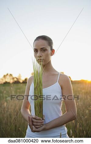 Young woman holding bundle of grass in field View Large Photo Image Stock Image - Young woman holding bundle of grass in field. Fotosearch