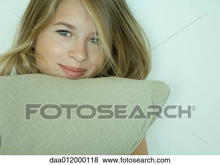 Stock Photo - Young woman holding cushion under chin, smiling at camera. Fotosearch