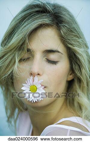 Stock Photograph - Young woman holding flower in mouth, eyes closed, portrait. Fotosearch