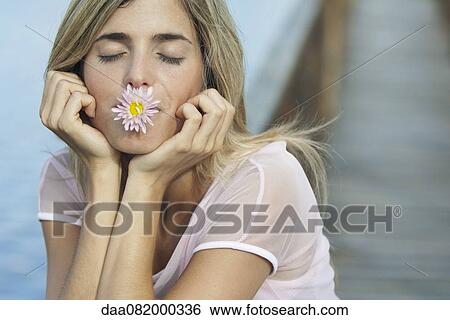 Stock Photograph - Young woman holding flower in mouth with eyes closed. Fotosearch