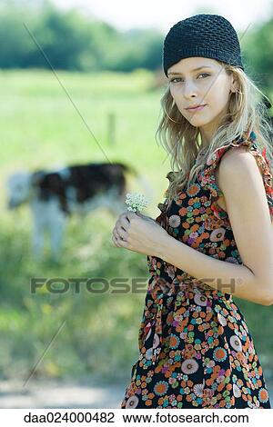 Young woman holding flower in rural setting, smiling at camera View Large Photo Image Stock Image - Young woman holding flower in rural setting, smiling at camera. Fotosearch