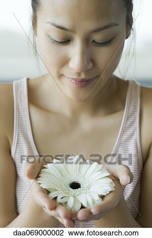 Stock Image - Young woman holding gerbera daisy, portrait. Fotosearch