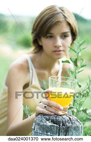 Young woman holding glass of orange juice on top of wood post View Large Photo Image Stock Image - Young woman holding glass of orange juice on top of wood post. Fotosearch