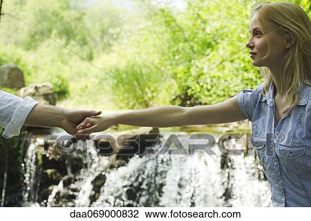 Stock Image - Young woman holding hands with boyfriend by waterfall, cropped. Fotosearch