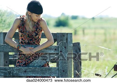 Young woman holding on to wooden fence, looking away View Large Photo Image Stock Image - Young woman holding on to wooden fence, looking away. Fotosearch