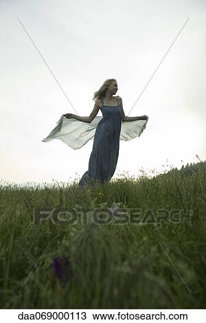 Stock Image - Young woman holding out scarf in breeze. Fotosearch