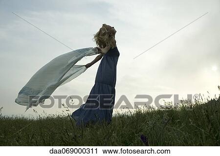 Stock Image - Young woman holding out scarf in breeze. Fotosearch