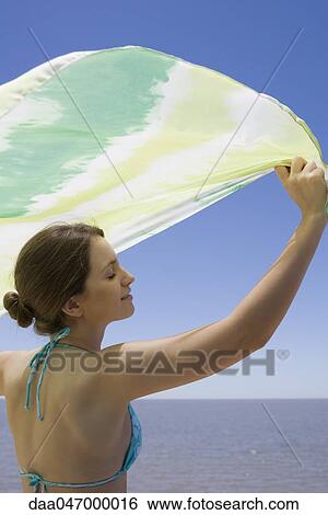 Young woman holding scarf in breeze, sea in background View Large Photo Image Stock Photograph - Young woman holding scarf in breeze, sea in background. Fotosearch