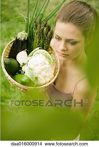 Young woman holding up basket full of vegetables View Large Photo Image Picture - Young woman holding up basket full of vegetables. Fotosearch