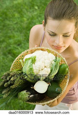 Young woman holding up basket full of vegetables View Large Photo Image Stock Image - Young woman holding up basket full of vegetables. Fotosearch