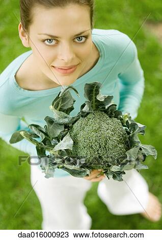 Stock Image - Young woman holding up broccoli. Fotosearch