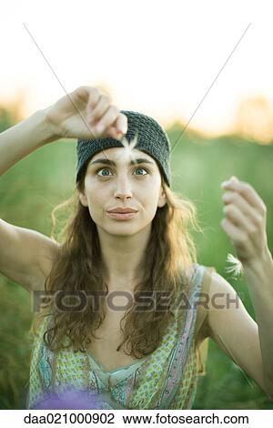 Stock Image - Young woman holding up dandelion seed head, crossing eyes. Fotosearch
