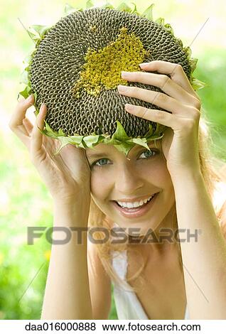 Stock Photo - Young woman holding up dried sunflower over head. Fotosearch