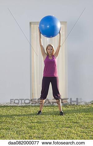 Young woman holding up fitness ball above head View Large Photo Image Stock Photo - Young woman holding up fitness ball above head. Fotosearch