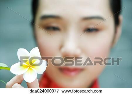 Stock Photo - Young woman holding up flower, close-up. Fotosearch