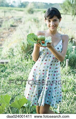 Stock Image - Young woman holding up fresh produce in cabbage leaves, smiling at camera. Fotosearch