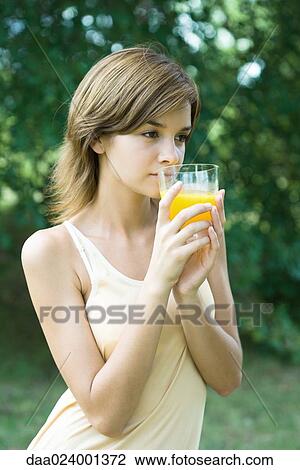 Young woman holding up glass of orange juice, looking out of frame View Large Photo Image Stock Image - Young woman holding up glass of orange juice, looking out of frame. Fotosearch