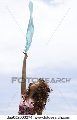 Picture - Young woman holding up scarf in wind. Fotosearch