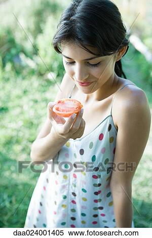 Stock Photography - Young woman holding up tomato half, smiling. Fotosearch