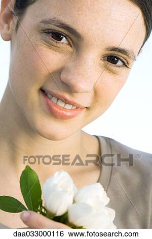 Young woman holding white flowers, smiling at camera View Large Photo Image Stock Photograph - Young woman holding white flowers, smiling at camera. Fotosearch
