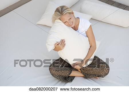 Young woman hugging pillow on bed, high angle view View Large Photo Image Stock Photo - Young woman hugging pillow on bed, high angle view. Fotosearch