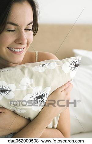 Stock Photo - Young woman hugging pillow, smiling with eyes closed. Fotosearch