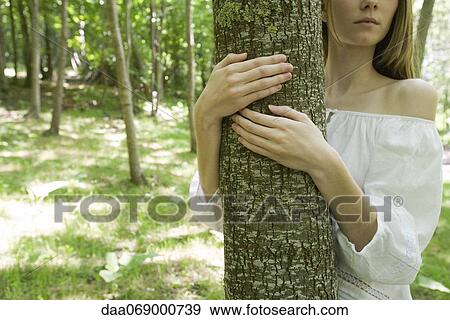 Stock Photo - Young woman hugging tree, cropped. Fotosearch