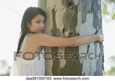 Young woman hugging tree trunk View Large Photo Image Stock Image - Young woman hugging tree trunk. Fotosearch