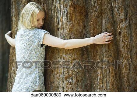 Stock Image - Young woman hugging tree trunk with eyes closed. Fotosearch