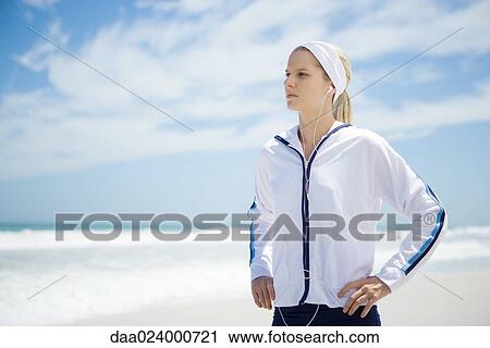 Young woman in active wear on beach, listening to earphones, hands on hips View Large Photo Image Stock Image - Young woman in active wear on beach, listening to earphones, hands on hips. Fotosearch