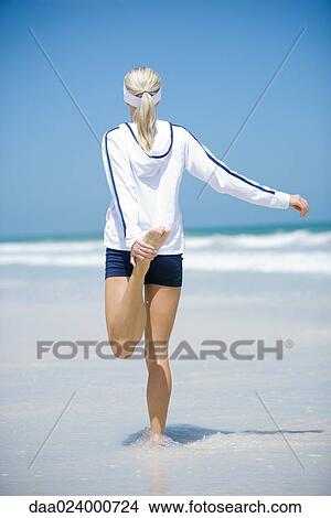 Young woman in active wear, stretching on beach, rear view View Large Photo Image Picture - Young woman in active wear, stretching on beach, rear view. Fotosearch