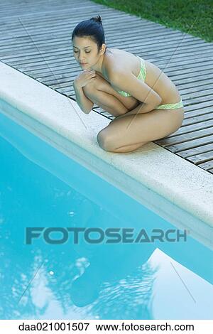 Young woman in bikini crouching by edge of pool View Large Photo Image Stock Photo - Young woman in bikini crouching by edge of pool. Fotosearch