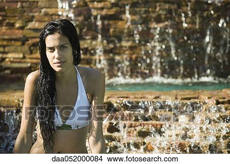 Picture - Young woman in bikini relaxing by waterfall. Fotosearch