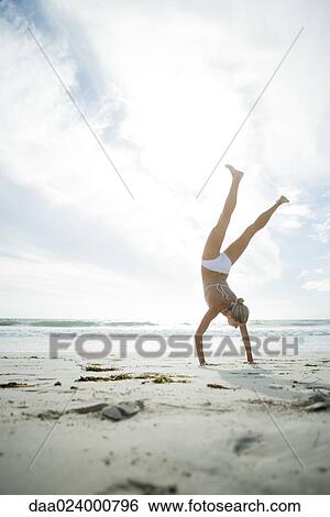 Young woman in bikini standing on hands on beach, full length View Large Photo Image Stock Photograph - Young woman in bikini standing on hands on beach, full length. Fotosearch