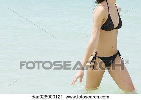 Young woman in bikini walking knee-deep in water, cropped view View Large Photo Image Stock Image - Young woman in bikini walking knee-deep in water, cropped view. Fotosearch